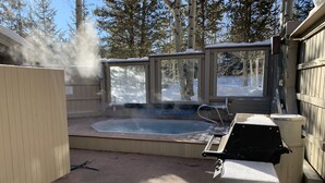 A hot tub with steam rising, surrounded by a wooden deck and a glass enclosure. - Cozy condo, Ski-in, one block from Main Street (Breckenridge)