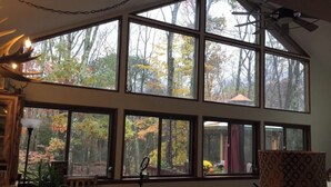 A room with multiple large windows offering views of trees and a forest. There is a ceiling fan, a lamp, and a patterned chair. - Relaxing Rustic ranch at Locust Lake!  with beautiful views!  Close to the Lake! (Pocono Lake)