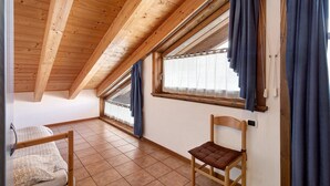 Una habitación con techo inclinado, una cama, una silla y ventanas con cortinas.