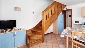 Una cocina con una escalera de madera, una mesa de comedor con mantel estampado y un televisor sobre un mueble.
