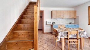 Una escalera de madera que lleva a una cocina con una mesa de comedor y sillas, armarios de madera y piso de baldosas.
