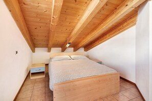 Een slaapkamer met een houten plafond, een bed, een nachtkastje en een klein dressoir.