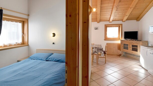 Ein Schlafzimmer mit Bett, einem fenster mit Vorhängen, einer Holzbalkendecke und einem kleinen Tisch mit Stuhl.