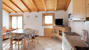 Eine Küche mit Holzbalken, einem Esstisch, Stühlen, einem Fernseher und einer Mikrowelle.