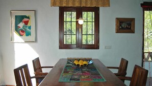A dining area with a wooden table, chairs, a colorful placemat, and a window with a view of greenery. - Frigiliana 010 (Frigiliana)
