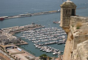 A marina with numerous boats docked, a stone tower, and a coastal cityscape.