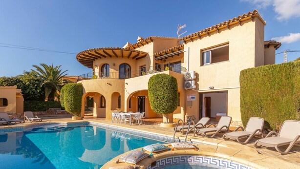 Uma área de piscina com espreguiçadeiras e um edifício com estilo arquitetônico mediterrâneo.