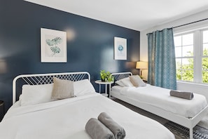 Une chambre d’hôtel avec deux lits simples, une petite table ronde agrémentée d’une plante et une fenêtre avec des rideaux.