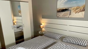 Una habitación de hotel con una cama, una mesita de noche, una lámpara, un espejo y una obra de arte en la pared con motivos playeros.