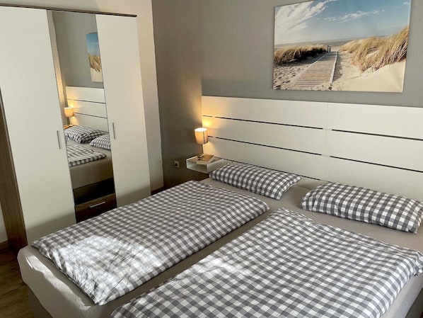 A hotel room with a bed, a nightstand, a lamp, a mirror, and a beach-themed wall art.