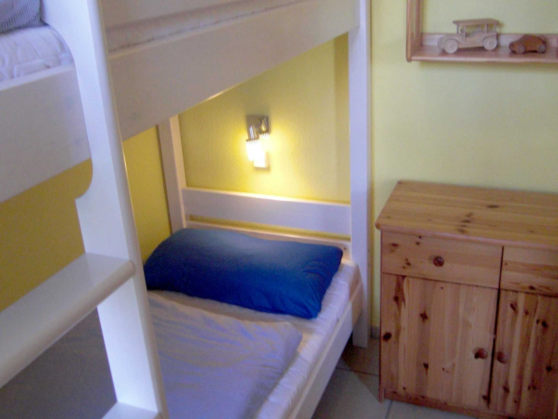 Un lit superposé avec un oreiller bleu et une commode en bois dotée de tiroirs.