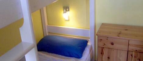 Un lit superposé avec un oreiller bleu et une commode en bois dotée de tiroirs.