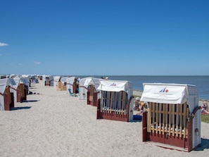 Beach huts with white canopies, arranged in rows along a sandy beach, with the sea in the background.