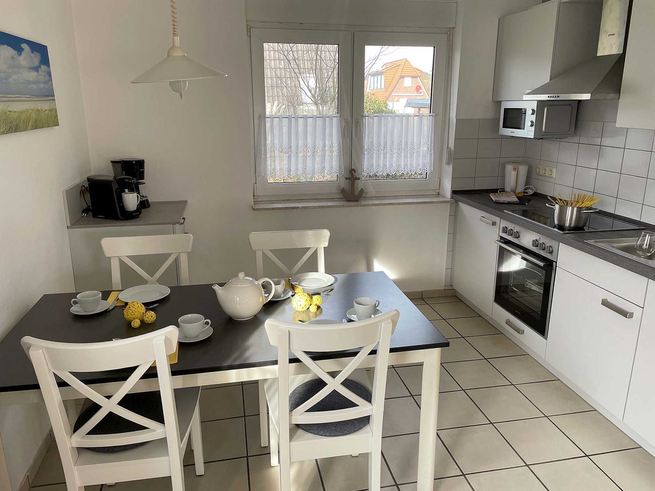 Une cuisine avec des meubles blancs, une cuisinière, un four à micro-ondes et une table à manger avec des chaises.
