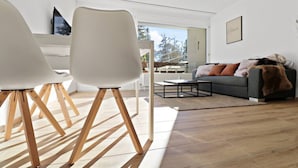 A modern living room with a sofa, coffee table, and two white chairs with wooden legs. - Cosy, renovated apartment in the heart of the resort (Crans-Montana)