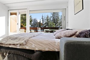 A bedroom with a large bed, a view of trees and a wooden deck outside. - Cozy, renovated apartment in the heart of the resort (Crans-Montana)