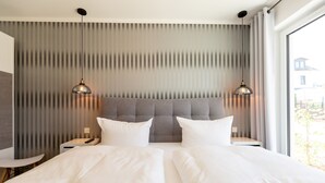 Una habitación de hotel moderna con una cama grande, dos mesitas de noche y un ventanal con cortinas.