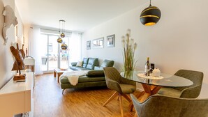 Una sala de estar moderna con una mesa de comedor de vidrio, sofá verde e iluminación colgante.