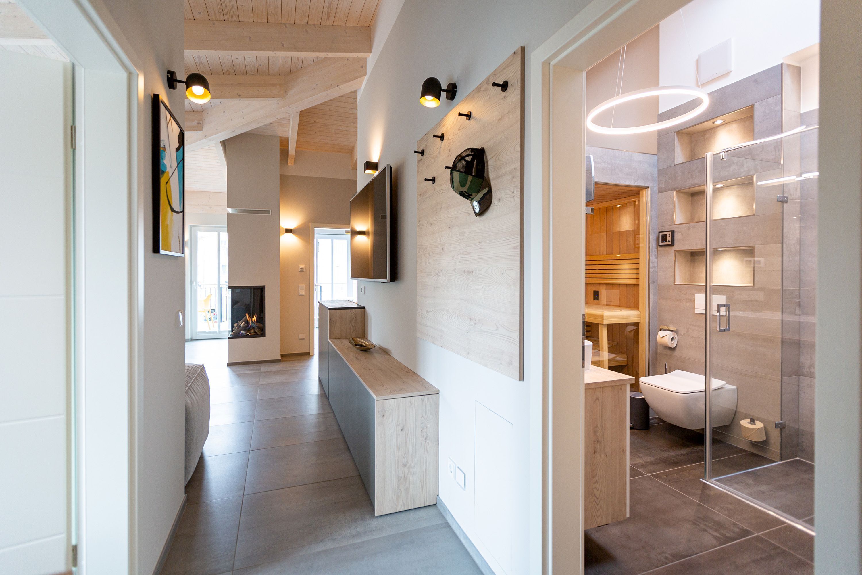 A modern interior with a wooden floor, a kitchen area with a counter, a mounted television, and a glass-enclosed shower area.