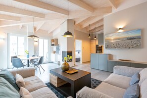 A modern living room with a sofa, coffee table, pendant lights, and a dining area with chairs and a table.