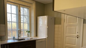 A kitchen with a marble countertop, a refrigerator, a dishwasher, and a window with a view of trees.