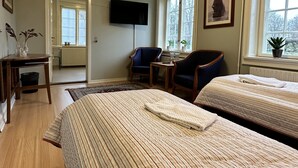 A hotel room with two beds, a desk, a chair, a television, and a window with a view of trees.