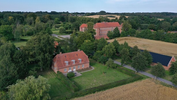 An aerial view of a large estate with multiple buildings, extensive greenery, and a well-maintained lawn.