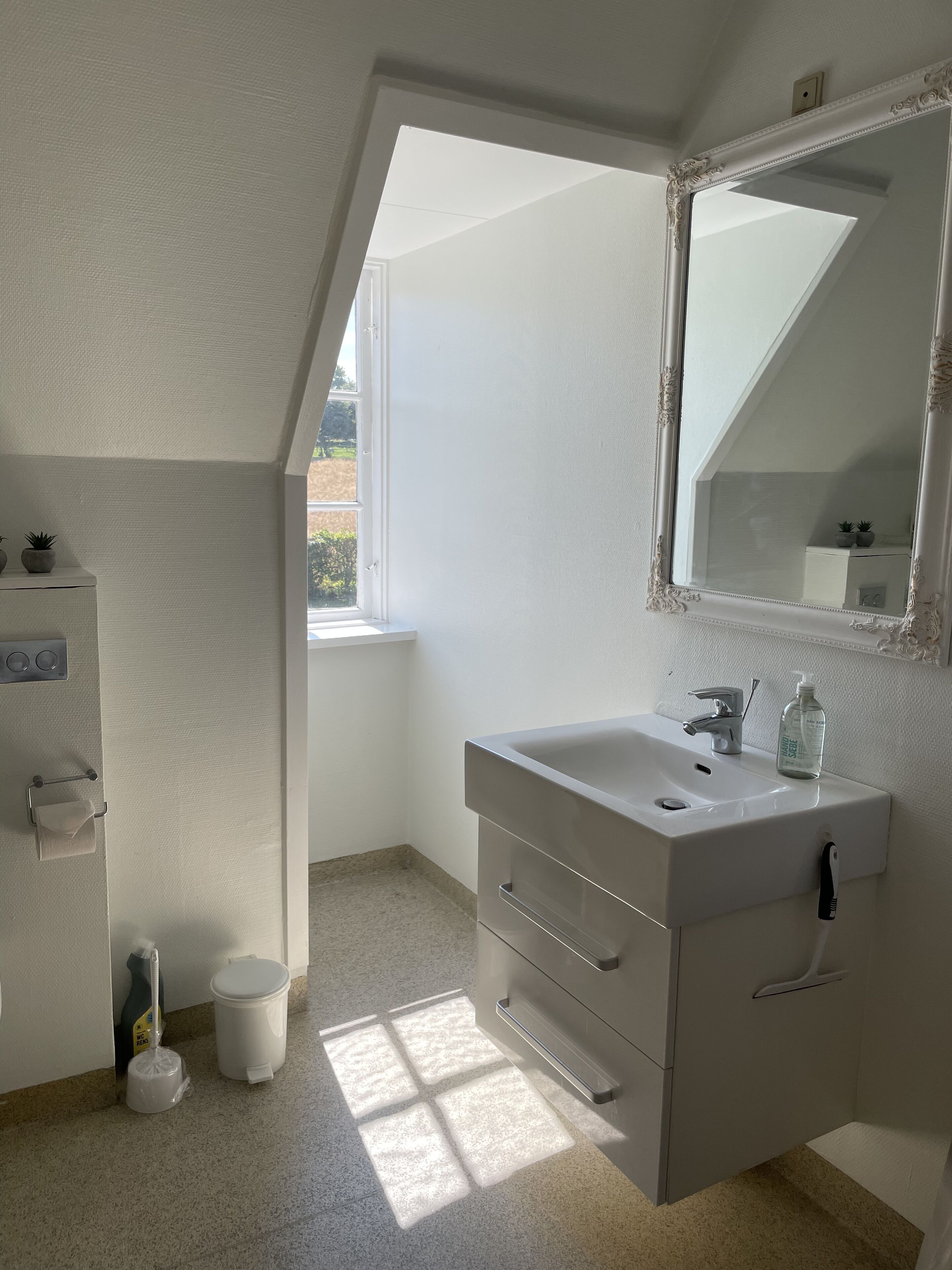 Un baño moderno con un tocador blanco, un espejo grande y una ventana que proporciona luz natural.