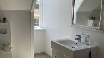 Un baño moderno con un tocador blanco, un espejo grande y una ventana que proporciona luz natural.