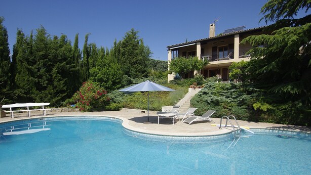 A swimming pool with lounge chairs and a sun umbrella, surrounded by lush greenery and a building with a balcony. - Beautiful view. (Valensole)