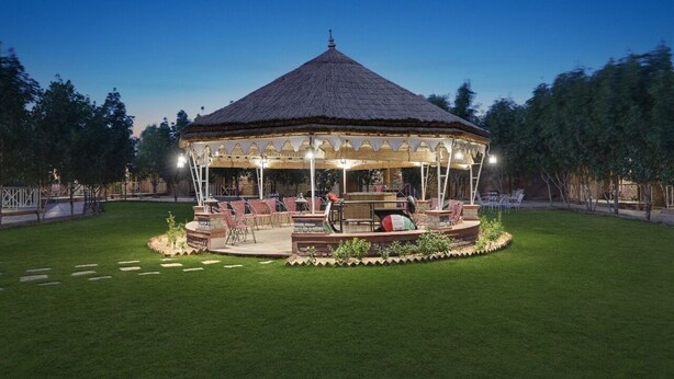 A gazebo with a thatched roof, surrounded by a well-maintained lawn and outdoor seating area.