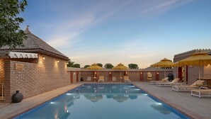 A swimming pool with lounge chairs and umbrellas, surrounded by brick walls and traditional architecture.