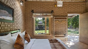 A bedroom with a brick wall, a bed with white linens, leopard print pillows, and a window with a view of the outdoors.