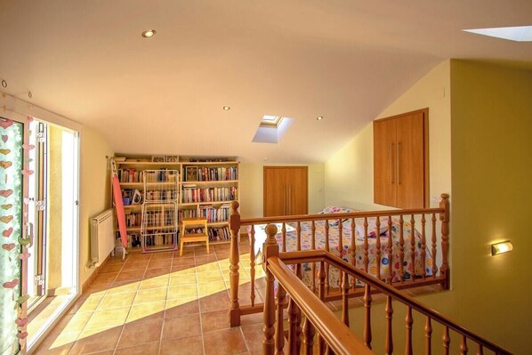 A spacious room with a wooden staircase, a large bookshelf, and a skylight.