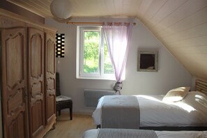 Quarto com teto inclinado, janela com vista para o verde, guarda-roupa de madeira, cama com roupa de cama listrada e uma cadeira.