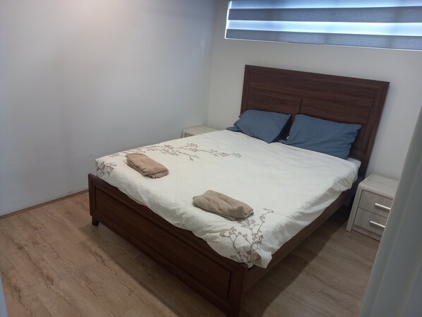 A neatly made bed with a floral bedspread and two pillows, a wooden headboard, and a small bedside table with drawers. - MODERN 2 BED APARTMENTS WITH WHEELCHAIR ACCESS (Kelmscott)