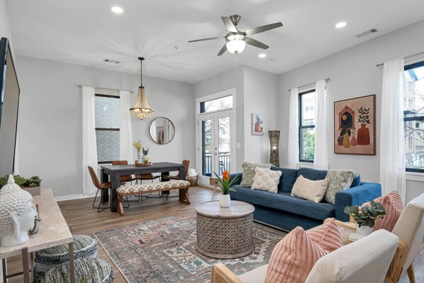 A spacious living room with a dark blue sofa, a round coffee table, and a dining area with a wooden table and chairs.