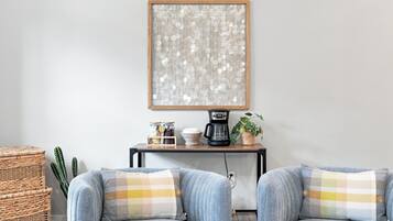 A living room with two grey armchairs, a coffee table, a wall-mounted artwork, and a cactus plant.