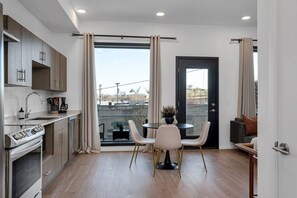 A modern kitchen with a dining area, a black door, and a view of buildings outside.