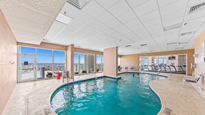 An indoor swimming pool with clear views of the cityscape through large windows. - Lighthouse 402 | Beachfront | Waterspouts + Zero Entry Pool | My Beach Getaways (Gulf Shores)