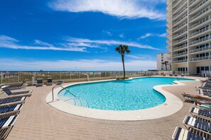A pool area with lounge chairs, a palm tree, and a view of the ocean.