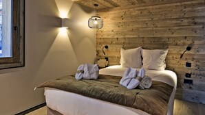 Une chambre avec un plafond en bois, un lit doté d’une tête de lit marron et une fenêtre située à gauche.