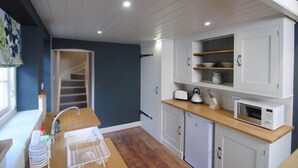 A compact kitchen with a wooden countertop, white cabinets, a built-in microwave, and a small sink. - Courtyard Cottages Lymington (Lymington)