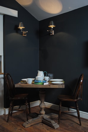A dining area with a dark wall, two chairs, a wooden table, and two wall-mounted lamps.