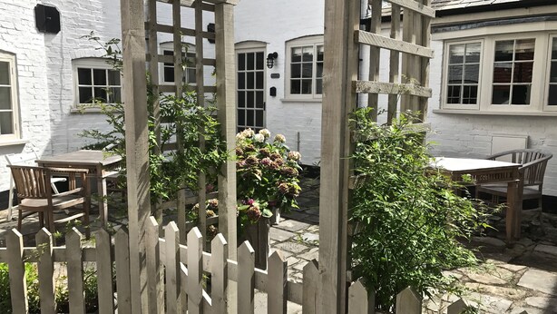 A courtyard with a wooden table and chairs, surrounded by white brick walls and a wooden fence. - Courtyard Cottages Lymington (Lymington)
