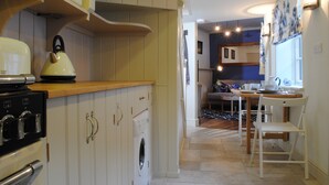 A kitchen with a stove, oven, and washing machine. There is a dining area with a table and chairs. - Courtyard Cottages Lymington (Lymington)