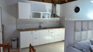 A compact kitchen with white cabinets, a wooden countertop, a stainless steel range hood, and a built-in shelving unit.