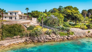 A coastal property with a stone wall, clear turquoise waters, and lush greenery.