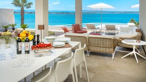 A terrace with a table set for dining, wicker furniture, and a view of the sea.