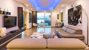 A modern living room with a large sofa, a flat-screen TV, and a dining area with chairs.